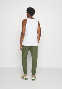 Top de tanque branco, calças de jogging verdes texturizadas e sapatilhas bege com detalhes coloridos. O conjunto apresenta um corte descontraído e punhos elásticos.