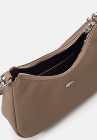 Sacoche en nylon marron avec une texture lisse, dotée d'une fermeture éclair en métal argenté et d'un petit logo en accent. Compartiment intérieur visible.