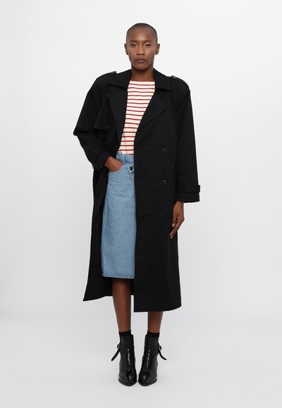 Trench coat negru cu nasturi cu două rânduri, asortat cu o cămașă în dungi și o fustă din denim. Botine cu un finisaj elegant și lucios.
