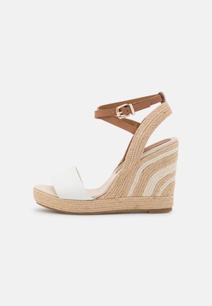 Sandale compensée avec talon tressé beige, bride avant blanche et bride de cheville marron réglable avec boucle sur fond blanc.