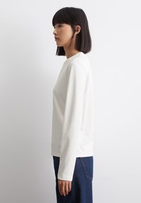 Hvid langærmet top lavet af glat stof, med en simpel rund halsudskæring og afslappet pasform, parret med mørkeblå jeans.