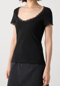 T-shirt nero a maniche corte con scollatura profonda bordata in pizzo e dettagli in pizzo sulle maniche. Materiale morbido, design aderente e orlo pulito.