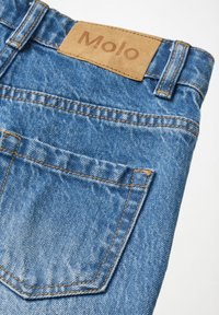 Κοντινό πλάνο μπλε τζιν παντελονιών που δείχνει την πίσω τσέπη και την καφέ δερμάτινη ετικέτα με το λογότυπο "Molo" ραμμένο στη μέση.