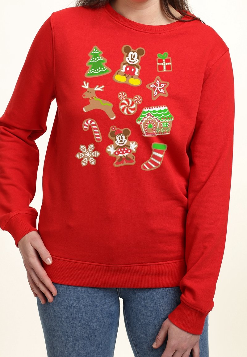 Personne portant un sweat rouge avec des biscuits en pain d'épices sur le thème de Noël, comprenant un arbre, un renne, un bâton de sucre d'orge, une chaussette et des figurines de souris de dessin animé.