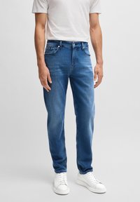 Ljust blå denimjeans med rak passform, fem fickor och en subtil blekning. I kombination med en enkel vit t-shirt och vita sneakers.
