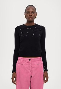 Maglione nero con scollatura tonda, decorato con perline argentate sul davanti. Abbinato a pantaloni in corduroy rosa con tasche laterali.