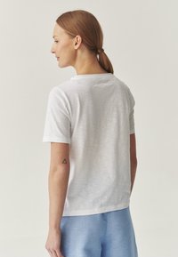 T-shirt bianco a maniche corte con vestibilità ampia e scollatura arrotondata, realizzato in tessuto leggero. Presenta un dettaglio della cucitura sul retro.