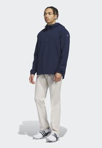 Granatowy hoodie z kapturem wykonany z teksturowanego materiału, z przednią kieszenią i elastycznymi mankietami, w połączeniu z kremowymi spodniami i białymi butami golfowymi.