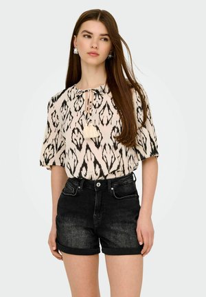 Blouse rose clair avec un motif abstrait noir, coupe ample, manches courtes, encolure nouée avec un gland. Associée à un short en denim noir taille haute.