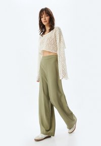Crop top en dentelle blanche avec un motif en diamant, associé à un pantalon ample vert olive. Le mannequin porte des baskets blanches. Design simple et minimaliste.