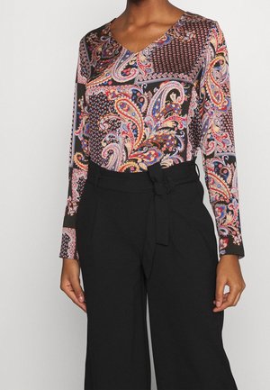 Maglia a maniche lunghe con un vivace motivo paisley su sfondo nero, abbinata a pantaloni neri a vita alta con cintura annodata.