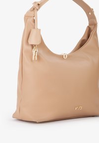 Beige leren hobo tas met een ronde vorm, gestructureerd oppervlak en hardware in goudkleur. Voorzien van een sleutelhanger en een reliëflogo.