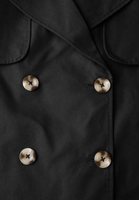 Czarny dwurzędowy płaszcz wykonany z tkaniny, z dużymi brązowymi guzikami w okrągłym wzorze i kieszeniami naszywanymi.