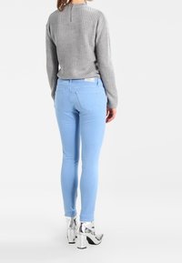 Jeans ajustados de color azul claro con una cintura alta, combinados con un suéter gris de canalé. La modelo lleva botas de plataforma plateadas y brillantes.