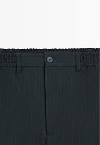 Pantaloni neri a righe sottili con vita elasticizzata, chiusura con bottone e tasche laterali. Il tessuto sembra liscio e strutturato.