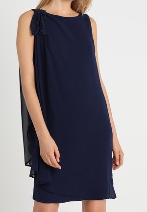 Marineblaues ärmelloses Kleid mit lockerem Schnitt, das eine Spitzen-Schleifen-Applikation auf einer Schulter und einen mehrlagigen Saum für zusätzlichen Effekt aufweist.