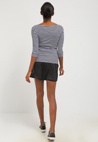 Svart satinkjol kombinerad med en marinblå och vit randig långärmad topp. Toppen har en figurnära design med trekvartsärmar och båtringning.