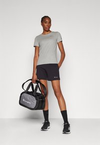 Camiseta gris de manga corta, pantalones cortos negros y una bolsa de gimnasio negra con detalles grises, que lleva la marca "Champion" y tiene asas estándar.