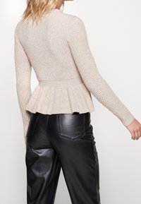 Pull en maille côtelée beige avec un ourlet peplum, des manches longues et un corsage ajusté, associé à un pantalon en cuir noir avec poches arrière.