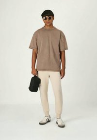 Behagelig beige oversized t-shirt med korte ærmer, parret med lysecreme joggers og hvide sneakers. Accessories inkluderer sorte solbriller og en lille taske.