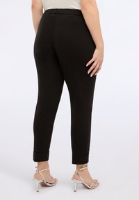 Pantaloni negri evazați cu talie elastică, având margini cu tiv; asociați cu sandale metalice cu toc înalt și bretele. Textură fină.