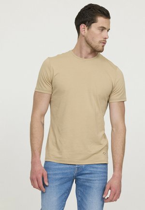 T-shirt beige à manches courtes en tissu lisse, présentant un col rond classique et un petit logo près de l'ourlet.