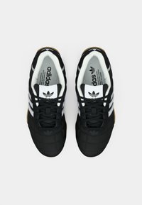 O pereche de pantofi sport negri Adidas cu dungi albe și logo, văzuți de sus pe un fundal simplu deschis.