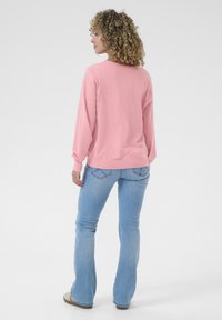 Felpa rosa chiaro con maniche lunghe, scollo rotondo e orlo a costine, abbinata a jeans svasati blu chiaro con cuciture nelle tasche posteriori.