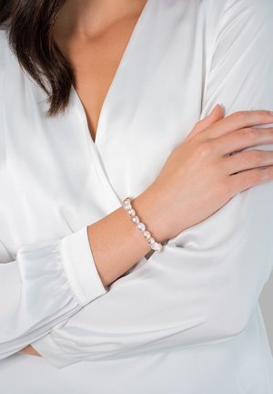 Pearl bracelet featuring alternating smooth white and peach beads, set on a flexible band, worn on a wrist with a white blouse.