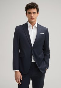 Giacca da uomo blu navy con vestibilità slim, rever a punta, due bottoni e due tasche frontali. Camicia bianca sotto con fazzoletto da taschino.