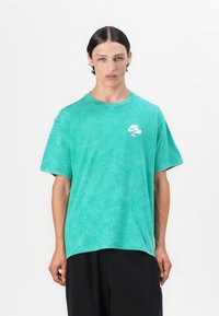 T-shirt verde, oversized, feita de algodão suave. Apresenta uma textura em degradê e um pequeno logótipo branco da Nike Air no lado esquerdo do peito.