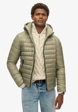 Olijfgroene pufferjack met horizontale stiknaden, een aansluitende capuchon en twee ritszakken. Draag het over een crèmekleurige kabelbrei trui en jeans.