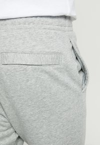 Grå sweatpants har en slät textur, elastisk midja och sidofickor. Inkluderar en sydd bakficka med en horisontell öppning.