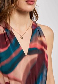 Blusa colorata e fluida con scollatura a V profonda. Presenta una combinazione di tonalità blu, bordeaux e beige con una morbida texture setosa. Include un dettaglio di collana dorata.