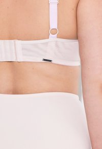 Light pink bra with mesh detailing, adjustable straps, and hook closure. The texture is smooth, and a small black label is visible.