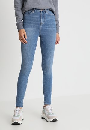 Jeans skinny de color azul claro, de denim, con cintura alta, que presentan un ligero desgastado y un estilo clásico de cinco bolsillos, combinados con zapatillas grises.