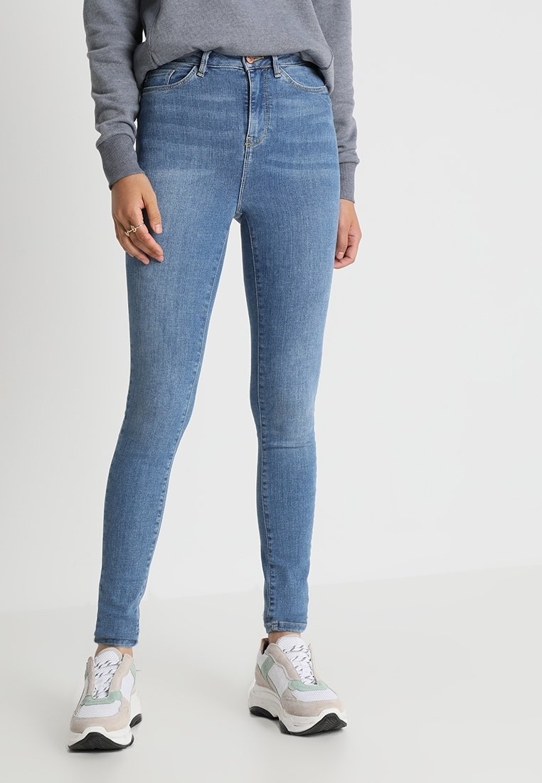 Světlé modré slim džíny vyrobené z denimu s vysokým pasem, s jemným vyblednutím a klasickým pětipocket stylem, doplněné šedými teniskami.