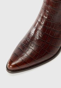 Brahno krokodil vzorovana usnjena gležnjak z usnjatim konico, ki se ponaša z elegantnim dizajnom in gladko površino, poudarjeno z diskretnimi šivi.