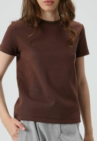 Braunes kurzärmeliges T-Shirt aus weicher Baumwolle mit Rundhalsausschnitt und regulärer Passform, kombiniert mit hellgrauen Hosen.