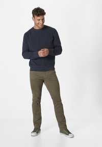 Marineblaue Sweatshirt mit runder Ausschnitt, gerippten Bündchen und Saum. Kombiniert mit olivgrünen Hosen und olivgrünen Sneakern mit weißen Sohlen.