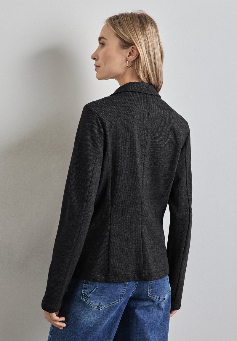 Černá ušitá sako s klopovým límcem, strukturovaná tkanina, slim fit. Model má na sobě volné modré džíny; zobrazeno zezadu a z boku.