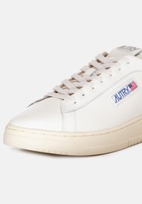 Sneaker bianco in pelle con suola in gomma beige, con dettagli grigi e logo. Lacci piatti e design aerodinamico.