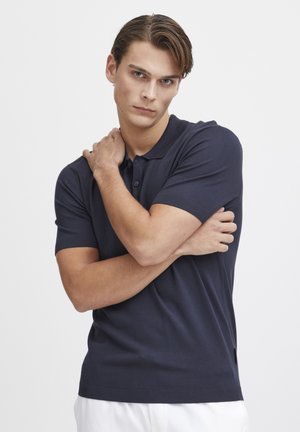 Navy polo shirt in a soft fabric with short sleeves, a collar, and a three-button placket. Features side slits at the hem for comfort.