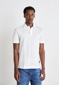 Hvit polo skjorte med et strukturert mønster, korte ermer og klassisk krage. Satt sammen med blå denim jeans.