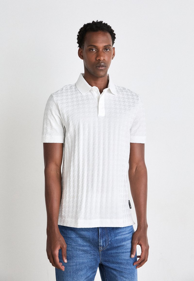 Hvit polo skjorte med et strukturert mønster, korte ermer og klassisk krage. Satt sammen med blå denim jeans.
