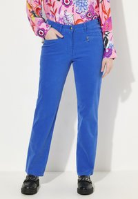 Blå kordfärgade byxor med rak bendesign, som har framfickor och dragkedjedetalj, ihop med en rosa blommig mönstrad skjorta.