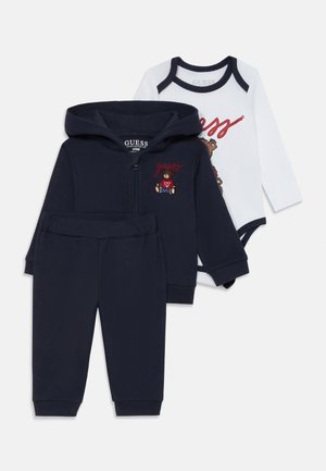 Tre-delt babyoutfit: navy zip-up hoodie med bjørnebroderi, matchende sweatpants og en hvid bodystocking med grafisk print og navy kant.