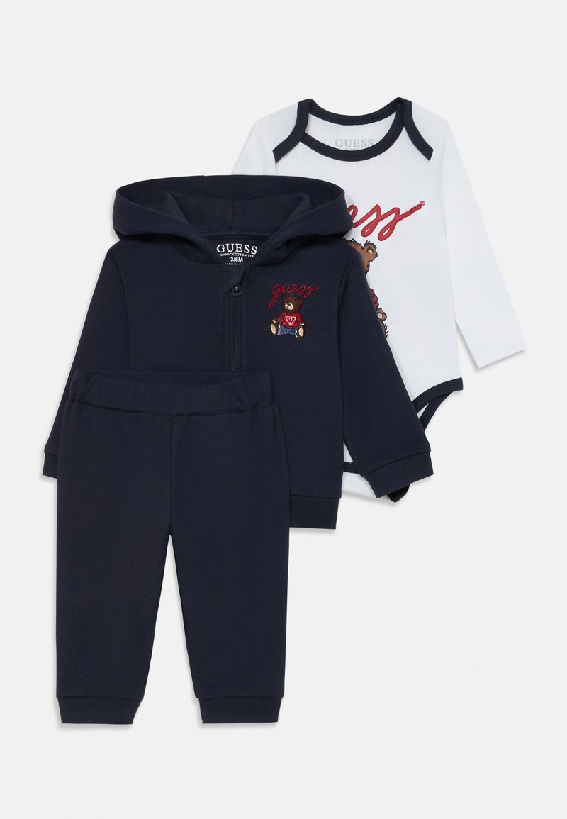Tre-delad babyoutfit: marinblå zip-up hoodie med björnbroderi, matchande sweatpants och en vit bodysuit med grafiskt tryck och marinblå kant.