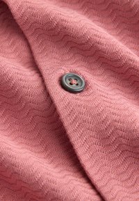 Tissu rose avec un motif en zigzag texturé et un seul bouton gris foncé à quatre trous cousu avec du fil rose visible en surface.