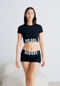 Juoda trumpa rankovė prie kelnių ir atitinkamų šortų, kuriuose yra balta "DIESEL" užrašas ant juosmens, prigludęs dizainas su lygiu audiniu ir trumpomis rankovėmis.